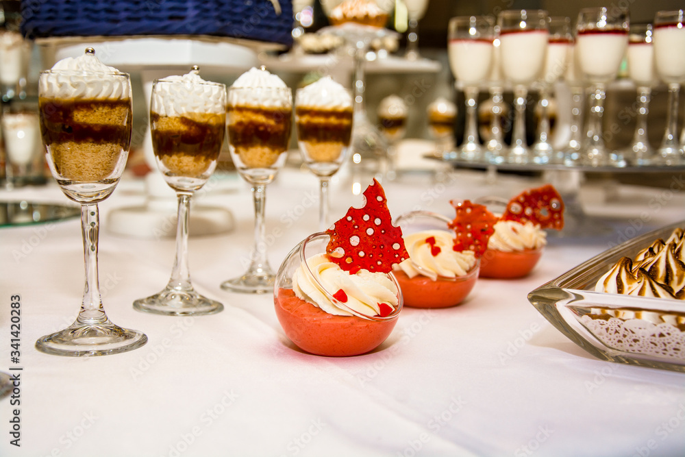 Candy bar with tasty desserts and appetizers at wedding reception. Decorated with flower compositions and candles. Sweet food, dessert, buffet, catering table, restaurant.