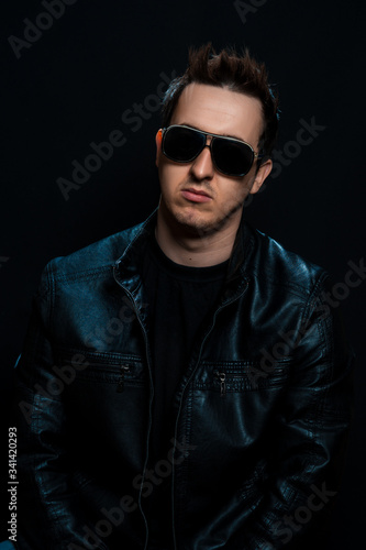 Young sexy stylish guy with glasses in a black leather jacket on a black background © TetianaRUD
