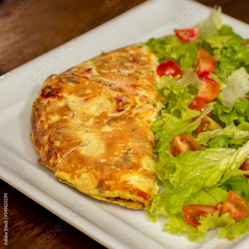 Omelette with tomatoes, cheese and green salad in white plate. 