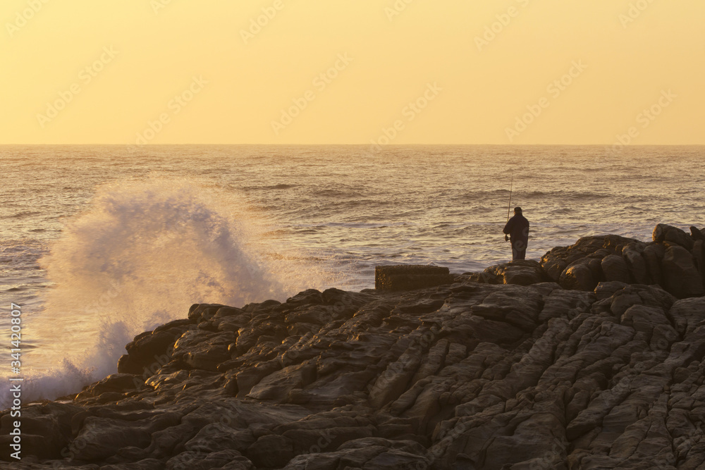 Fisherman at sunrise standing on the rocks