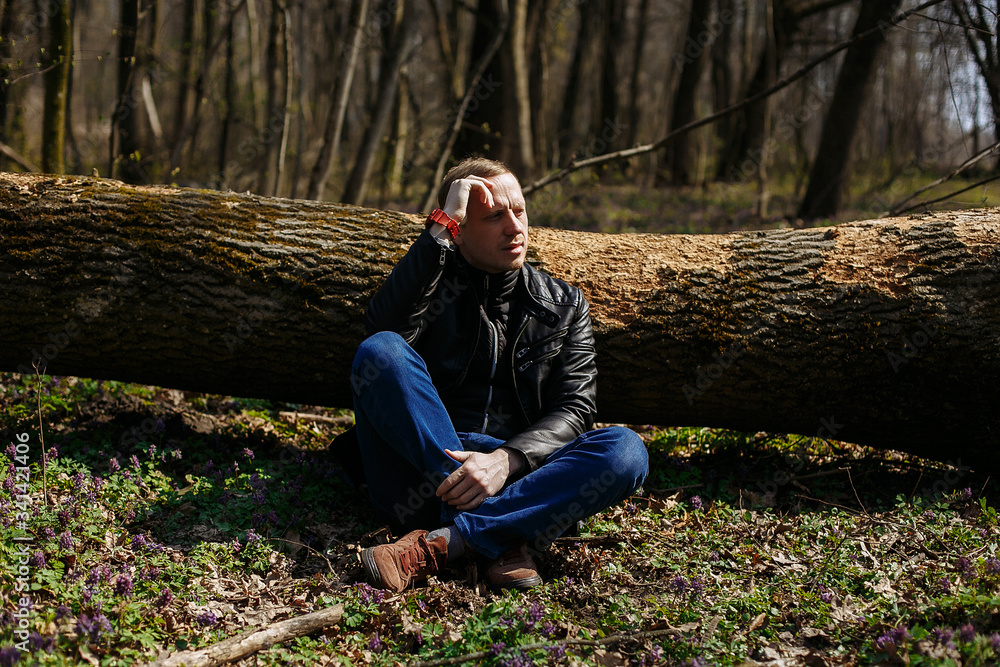 Young guy sits under a tree in the forest Young guy sits under a tree in the forest