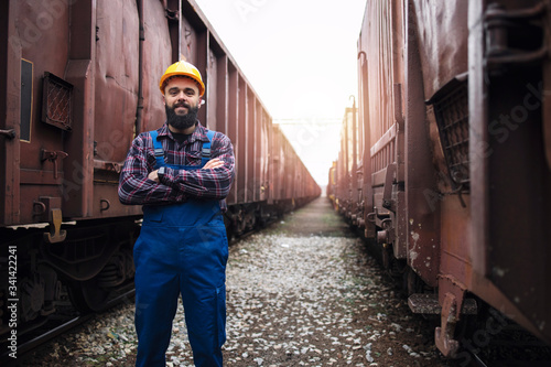 Portrait of railroad worker with crossed arms proudly standing at train station between wagons. Railroad freight transportation. photo