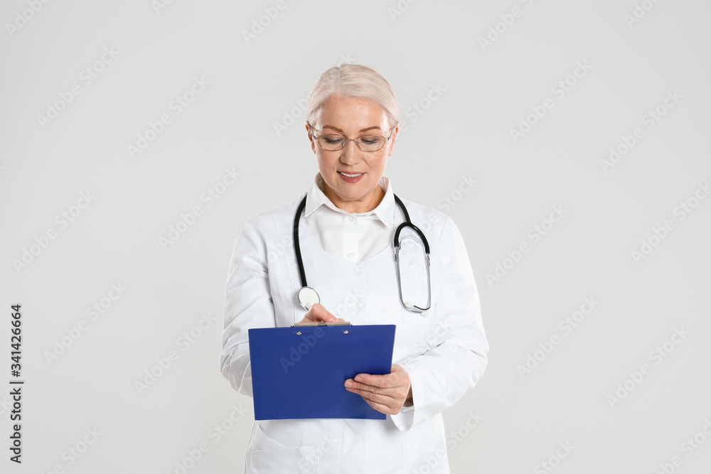 Mature doctor with clipboard on light grey background Mature doctor with clipboard on light grey background