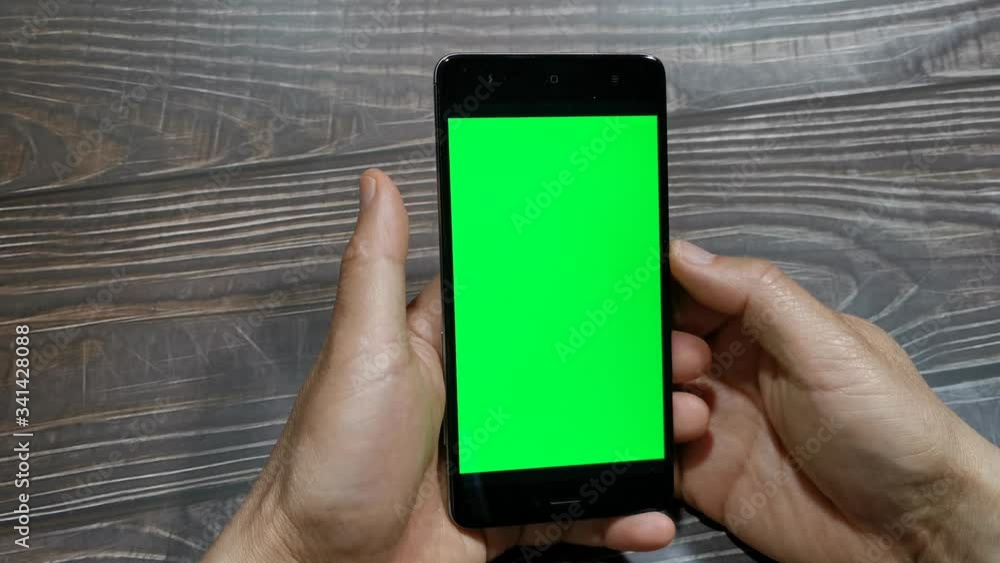 Close-up of man hands using smartphone with green screen. Close up video of man's hands reading news and looking social media web pages on mobile phone. Chroma key. Vertical Close-up of man hands using smartphone with green screen. Close up video of man's hands reading news and looking social media web pages on mobile phone. Chroma key. Vertical