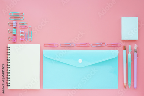 notebook, plastic envelope, stickers, pens and paper clips of pastel shades on a pink table.