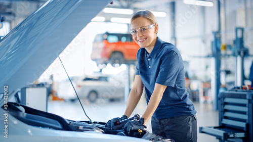 Beautiful Empowering Female Car Mechanic is Posing in a Car Service. She Wears Safety Glasses. Specialist Looks at a Camera and Smiles.