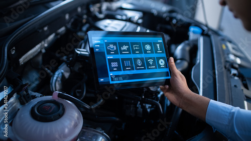 Car Service Manager or Mechanic Uses a Tablet Computer with a Futuristic Interactive Diagnostics Software. Specialist Inspecting the Vehicle in Order to Find Broken Components In the Engine Bay. photo