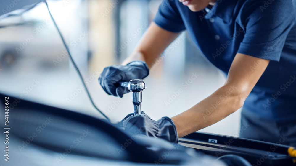 Close Up Shot of a Female Mechanic Working on a Car in a Car Service. Empowering Woman Makes an Usual Car Maintenance. She's Using a Ratchet. Modern Clean Workshop. Close Up Shot of a Female Mechanic Working on a Car in a Car Service. Empowering Woman Makes an Usual Car Maintenance. She's Using a Ratchet. Modern Clean Workshop.