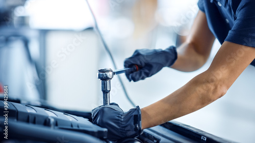Close Up Shot of a Female Mechanic Working on a Car in a Car Service. Empowering Woman Makes an Usual Car Maintenance. She's Using a Ratchet. Modern Clean Workshop.  © Gorodenkoff
