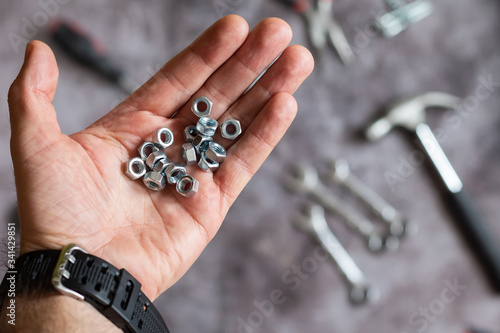 Many bolt nuts are in hand. Hands with tool. Set of tools for home repair. Hammer, pliers, nails, nuts.
