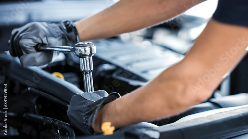 Close Up Shot of a Professional Mechanic Working on Vehicle in Car Service. Engine Specialist Fixing Motor. Repairman is Wearing Gloves and Using a Ratchet. Modern Clean Workshop.  photo