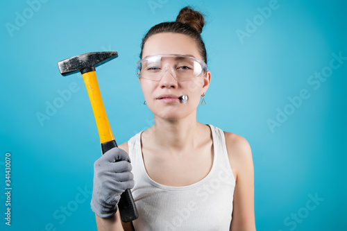 Obraz na płótnie Young woman squints, holding a hammer and nails in her mouth