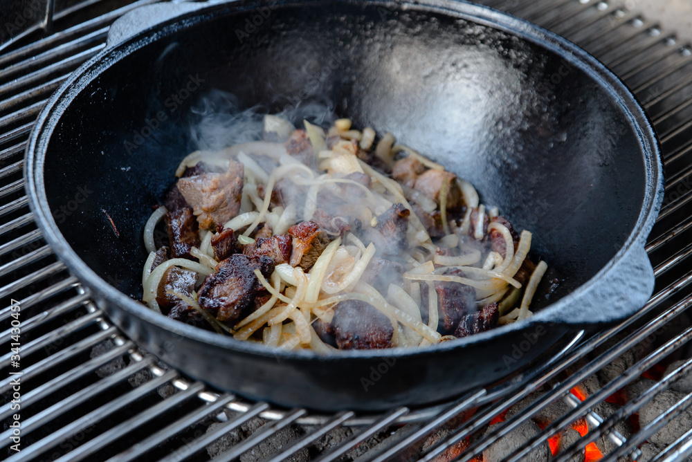 Pieces of lamb with onion are fried in boiling oil on the fire. As a stage in the preparation of traditional pilaf.step-by-step process of cooking pilaf in a cast iron cauldron on grill. Pieces of lamb with onion are fried in boiling oil on the fire. As a stage in the preparation of traditional pilaf.step-by-step process of cooking pilaf in a cast iron cauldron on grill.
