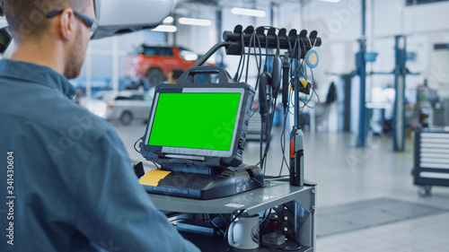 Car Service Mechanic is Running a Diagnostics Software on an Advanced Computer with Green Screen. Specialist Inspecting the Vehicle in Order to Find Broken Components and Errors in Data Logs.