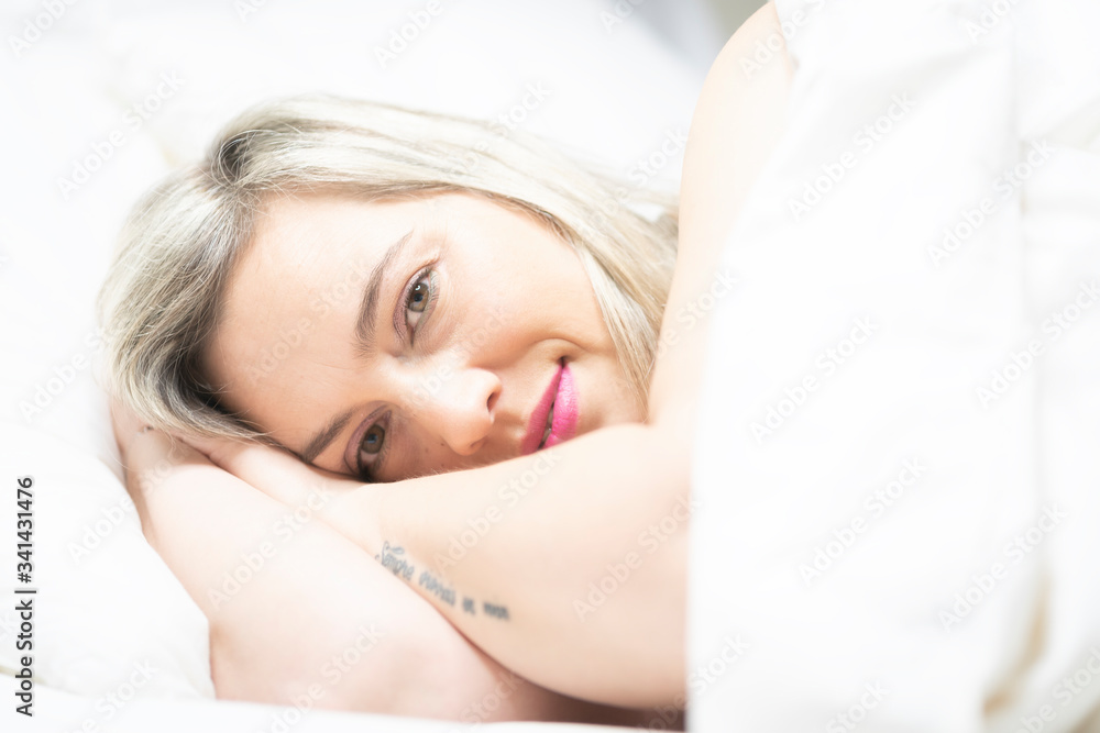 Fototapeta premium Portrait of an attractive woman smiling in a bed with white clothes