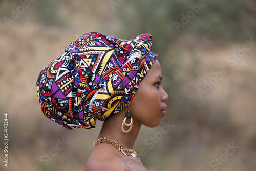 Profile portrait of a young dark-skinned African girl in a national headdress and gold jewelry photo