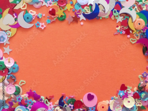 Orange background with a frame of sequins and confetti in the shape of a heart, stars, moons, etc.