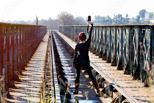Mujer de espalda  de pelo rojo en vía de tren abandonada levantando  cámara fotográfica  al cielo photo
