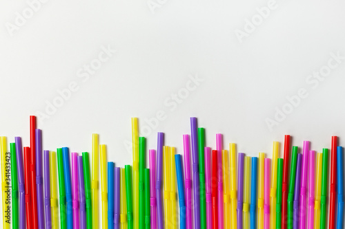 Disposable plastic multicolored tubules for drinks lined up in row on white background, copy space. Festive concept, party, birthday. Flat lay, top view. Horizontal