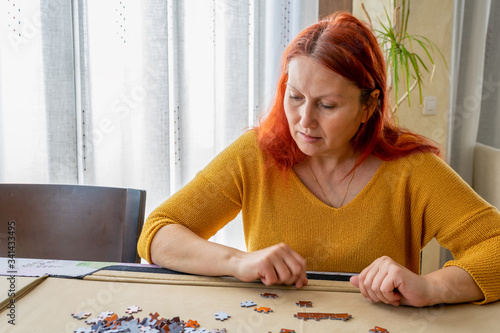 Beautiful redhead woman in a yellow sweater doing a puzzle in the living room at home