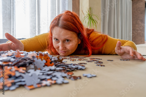 Beautiful redhead woman in a yellow sweater doing a puzzle in the living room at home