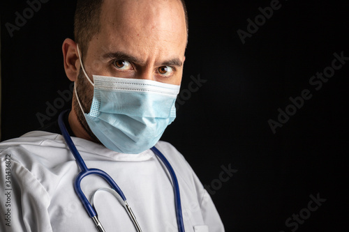 Portrait of a male doctor wearing a mask and a stethoscope against a seemless black background