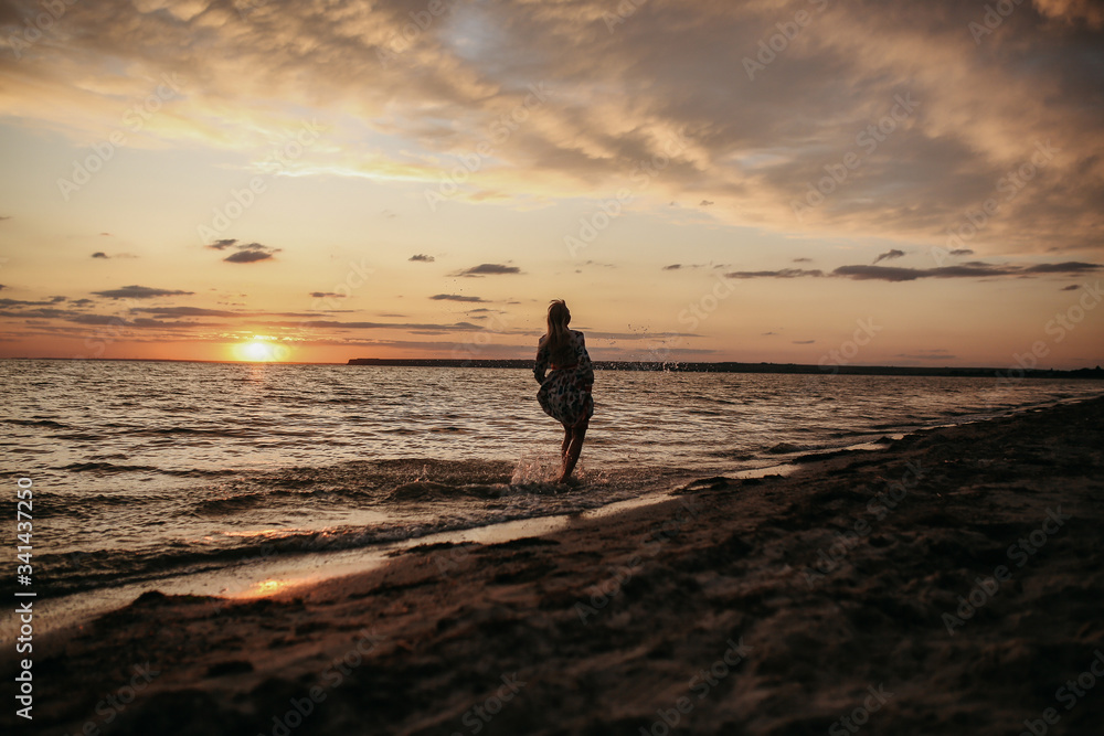 Fototapeta premium blonde girl walk along the beach by driving at sunset in a beautiful dress, beautiful evening on the river, beautiful sunset
