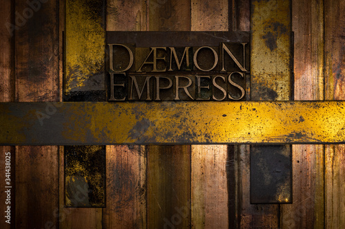 Photo of real authentic typeset letters forming Daemon Empress text on vintage textured grunge copper and gold background