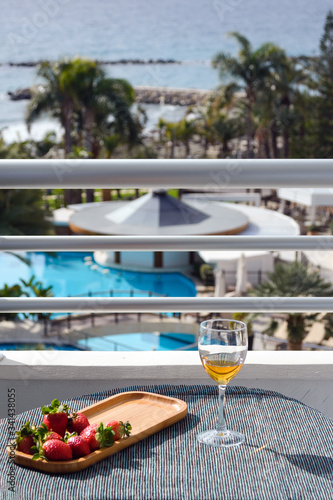 A glass of white wine stands on a table on the hotel balcony overlooking the pool and sea. Time relax.