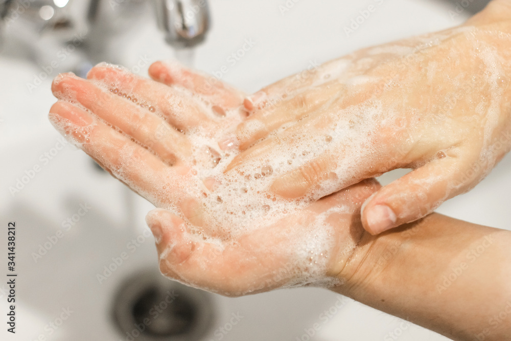 Fototapeta premium Washing hands. Rubbing palms, washing hands with antibacterial soap and in proper technique on background of flowing water in white bathroom. Prevention coronavirus. Cleaning and disinfecting hands