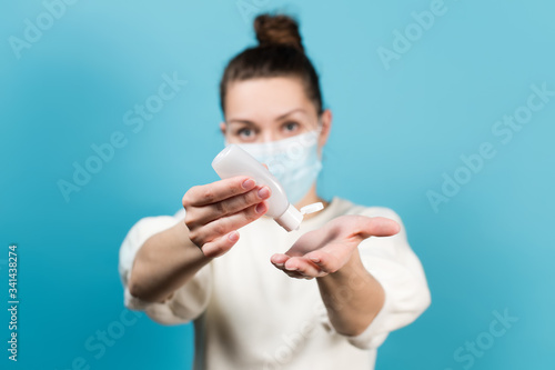 female in a medical mask squeezes a disinfectant into the palm of her hand