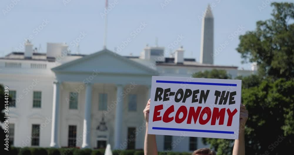 A man holds a RE-OPEN THE ECONOMY protest sign in front of the White House. The economy was mostly shut down during the COVID-19 pandemic of 2020. A man holds a RE-OPEN THE ECONOMY protest sign in front of the White House. The economy was mostly shut down during the COVID-19 pandemic of 2020.
