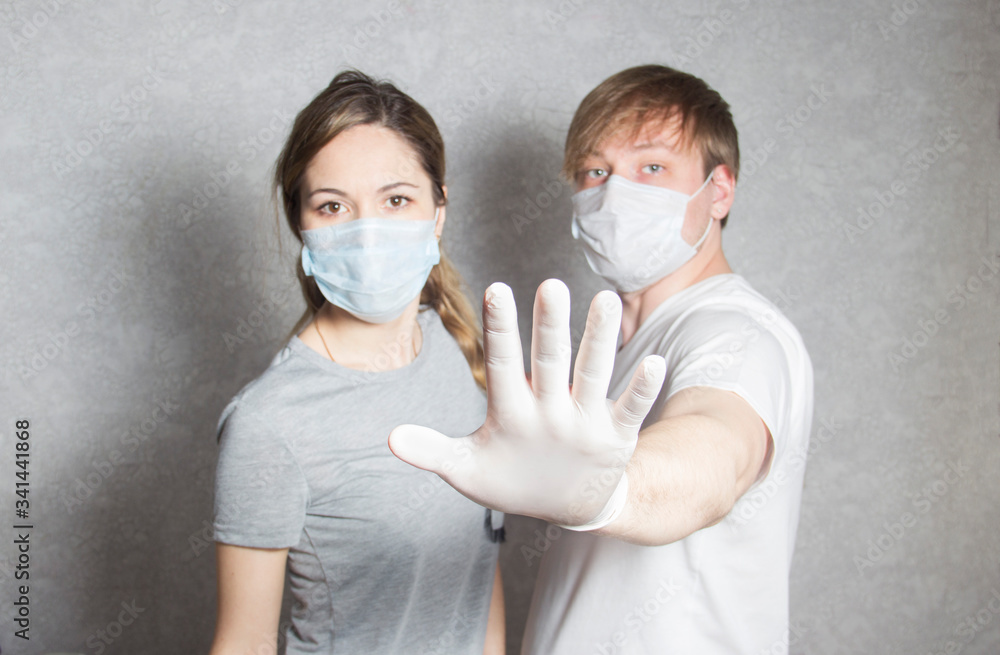 A man and a woman in masks and gloves show the stop. A man in a medical mask shows a hand gesture keep your distance. Selective focus.