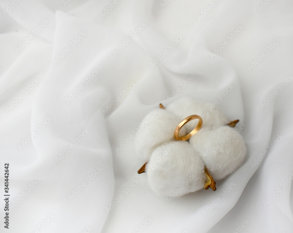 Elegant wedding concept. Golden ring with cotton flower pillow on white silk background. Feminine still life composition. Minimalist style. Copyspace. Elegant wedding concept. Golden ring with cotton flower pillow on white silk background. Feminine still life composition. Minimalist style. Copyspace.