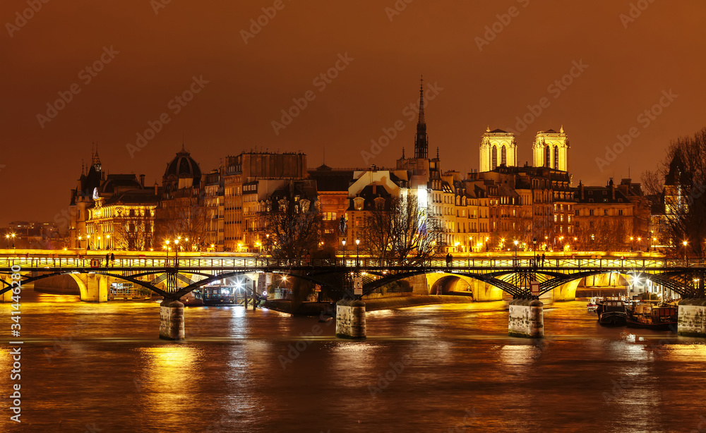 Bridge of Arts on the background of the island of Cite at night. Notre Damm is seen from behind the rooftops of the Cite island neighborhoods.