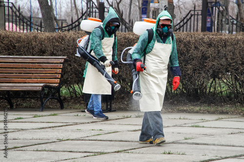 Workers in chemical protection suits decontaminate a city street or park during quarantine and a pandemic. Antiviral Fluid Spray