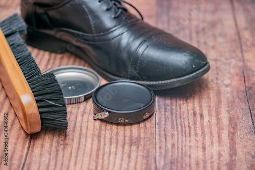Close up of shoe polish, cleaning brush and leather shoe on a wooden floor