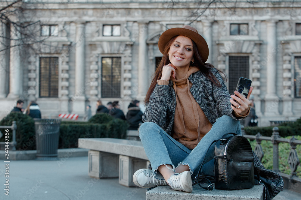 Girl in a fashionable brown hat smiles and takes a selfie.