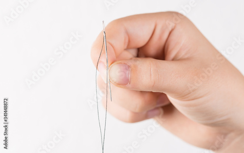 Detail of hand holding needle with thread on white background