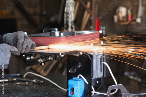 Industrial tool worker grinds a square steel pipe on a rotating belt sander