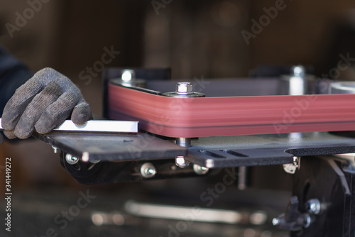 Industrial tool worker grinds a square steel pipe on a rotating belt sander