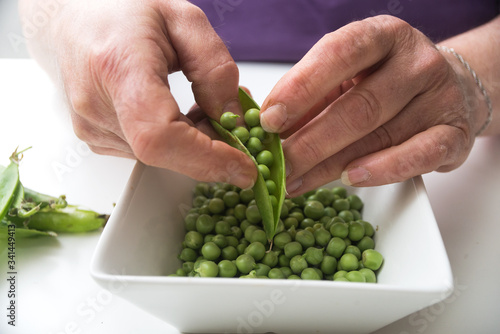 Closeup of hands of woman peeling fresh organic peas on white table background