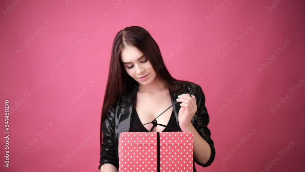 young woman in studio on a pink background with a wrapped gift young woman in studio on a pink background with a wrapped gift