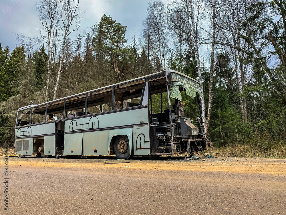 An old gray bus is abandoned on a road in the woods. Forest landscape with forgotten vintage gray bus. shattered commercial vehicle by the roadside