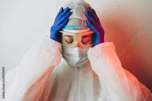 Doctor in protective uniform, reperitor, glasses, gloves on a blue background in neon light. A close-up portrait of a doctor in red neon. A tired man is battling a coronavirus. COVID 19 photo