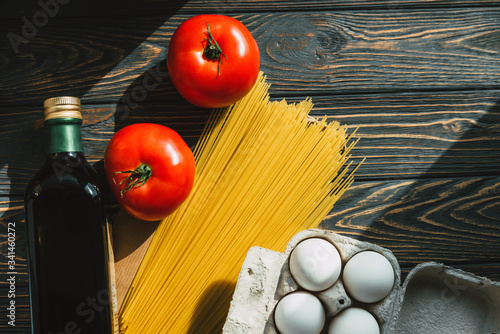 Products on the table. Pasta, olive oil in a bottle, tomatoes and eggs on a wooden background. Ingredients for cooking. Close-up