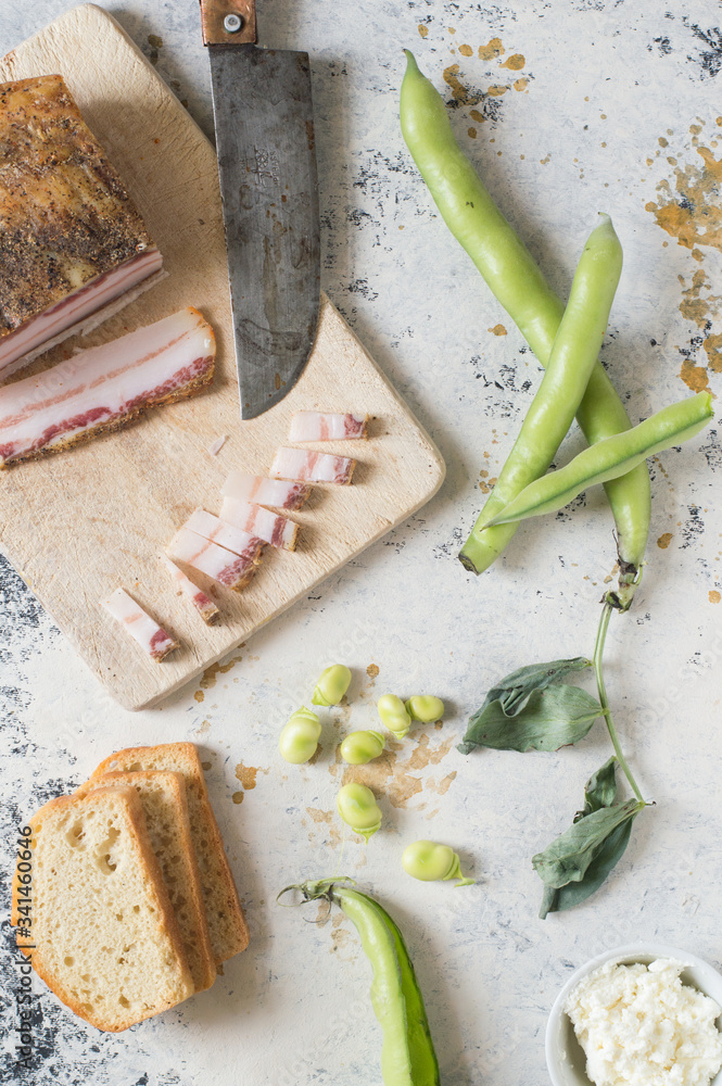 Broad beans, italian pancetta on a wooden chopping board. Three slice