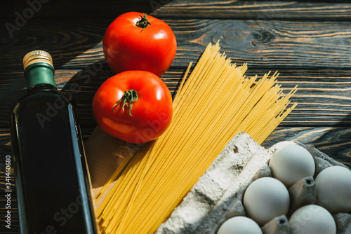 Products on the table. Pasta, olive oil in a bottle, tomatoes and eggs on a wooden background. Ingredients for cooking. Close-up