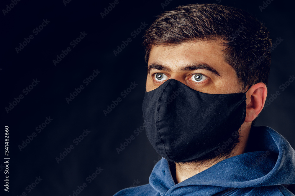 Portrait of handsome man wearing medical black mask on the face during virus epidemic lockdown posing on dark wall. Close up.