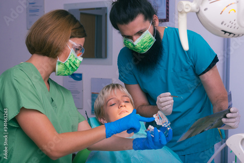 Young female and male dentists showing to their patient an X-ray picture of her teeth and a prosthetic jaw